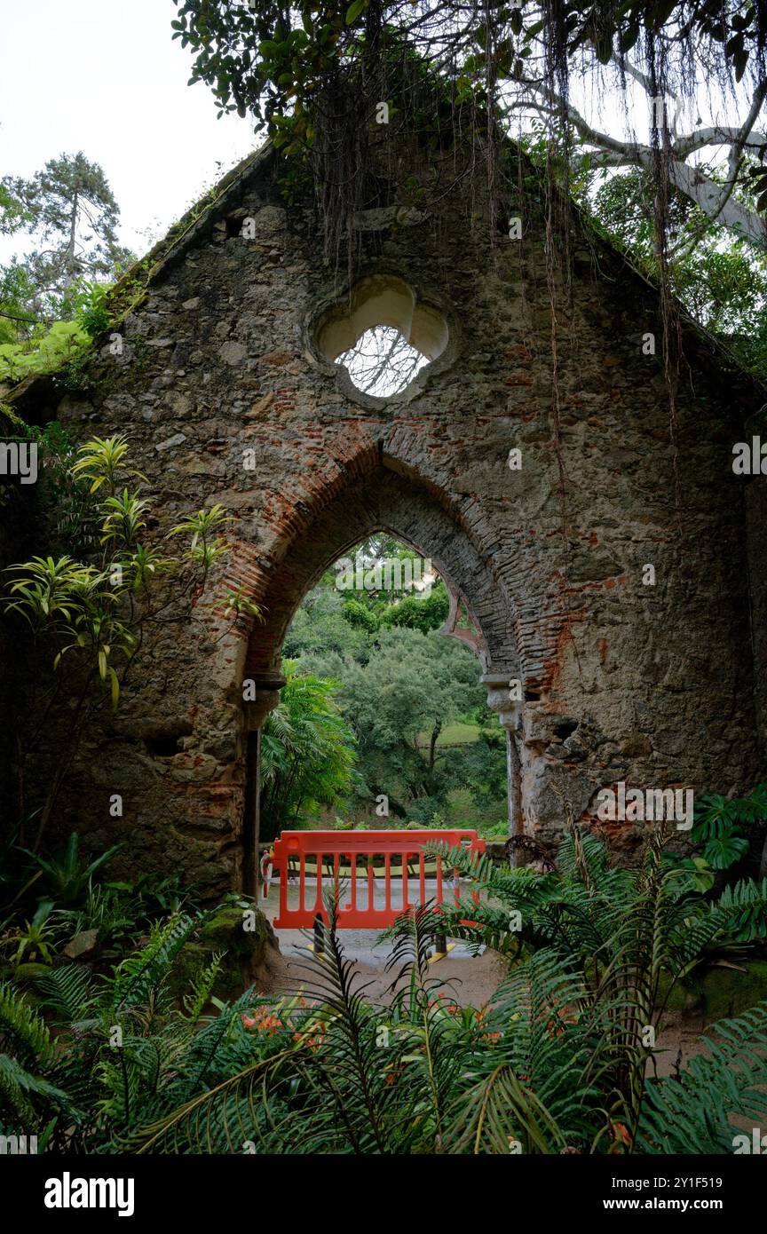 Antica arcata in pietra che conduce ad una vibrante vista del giardino incorniciata da lussureggiante vegetazione Foto Stock