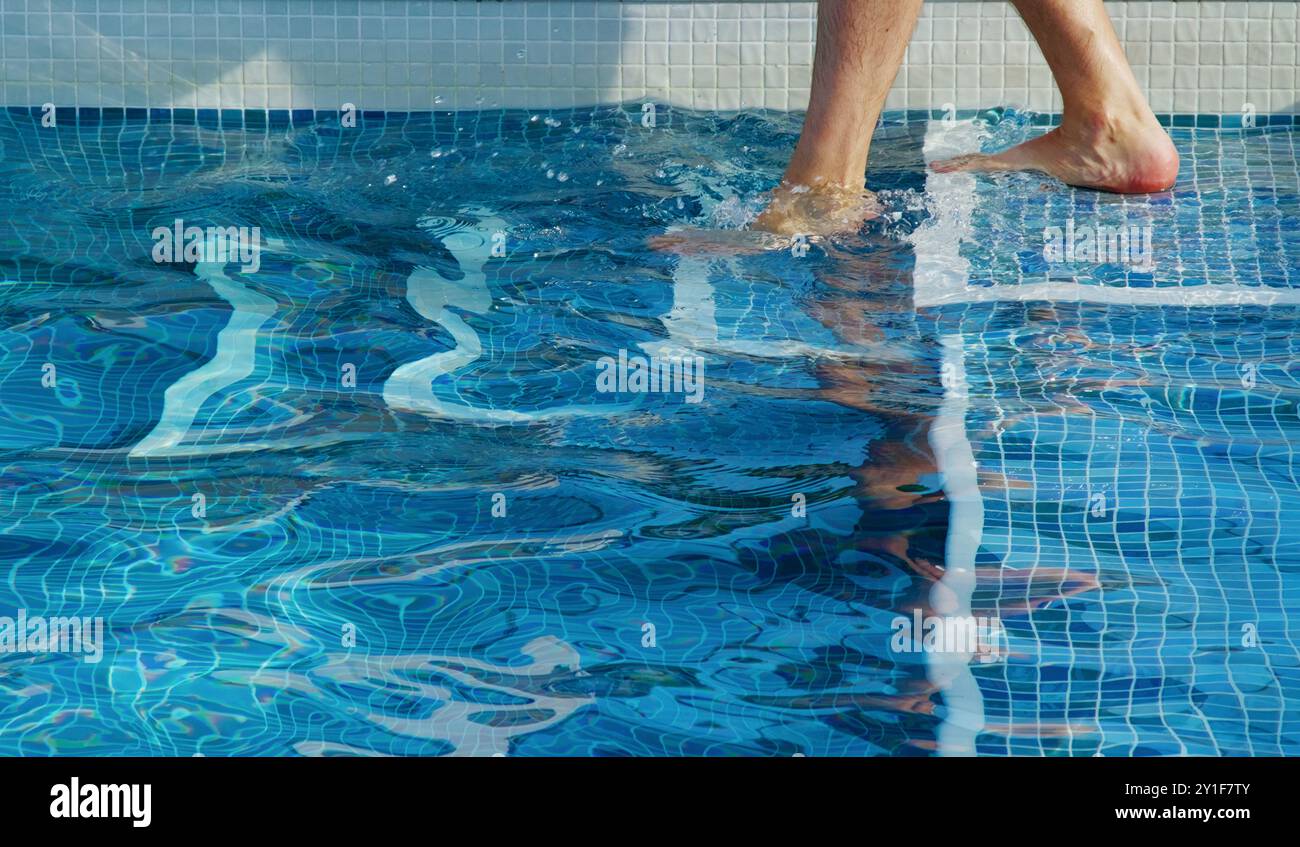 Gambe e piedi di un uomo che entra in Una piscina con piastrelle blu da Steps, Regno Unito Foto Stock