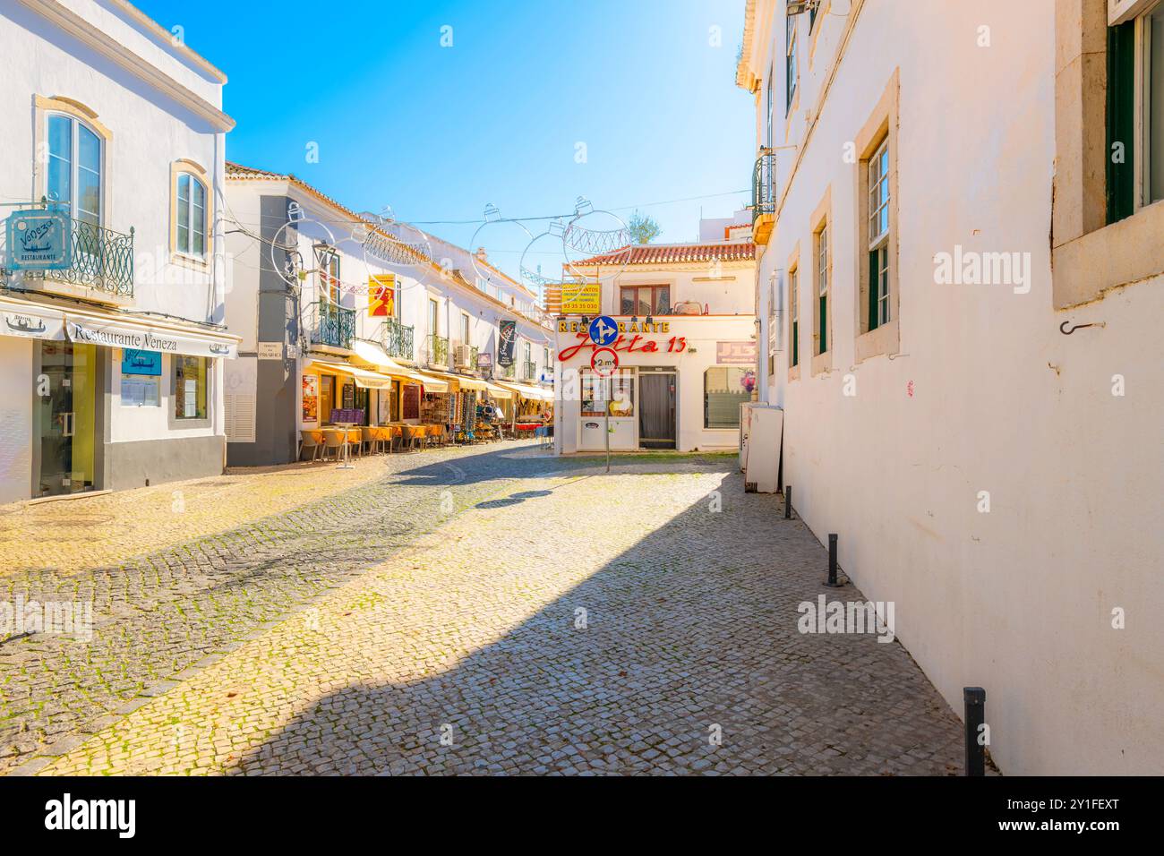 Una piccola piazza con negozi, caffetterie marciapiede e mercati nella storica città vecchia della città di mare imbiancata di Lagos, regione dell'Algarve del Portogallo. Foto Stock