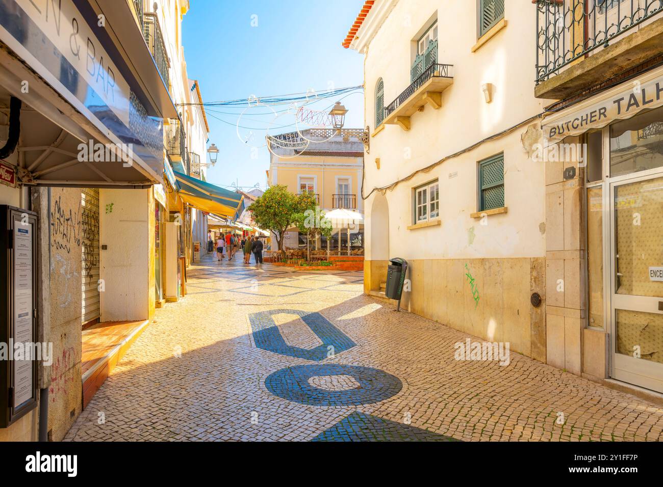Una strada pittoresca con i tradizionali modelli portoghesi di pavimentazione e caffetterie sul marciapiede a Lagos, Portogallo, nella regione dell'Algarve. Foto Stock
