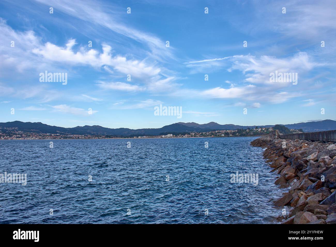 Vista mozzafiato dalla spiaggia di Barbeira a Bayona, Pontevedra, Spagna. L'immagine presenta un'aspra frangiflutti ricoperti di rocce che si estendono nella calma Foto Stock