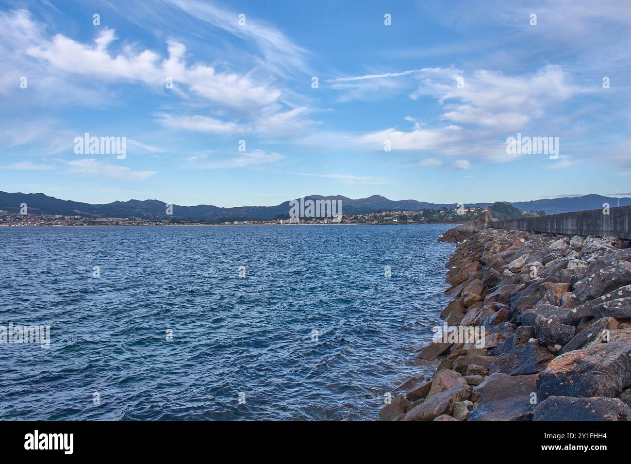 Vista mozzafiato dalla spiaggia di Barbeira a Bayona, Pontevedra, Spagna. L'immagine presenta un'aspra frangiflutti ricoperti di rocce che si estendono nella calma Foto Stock