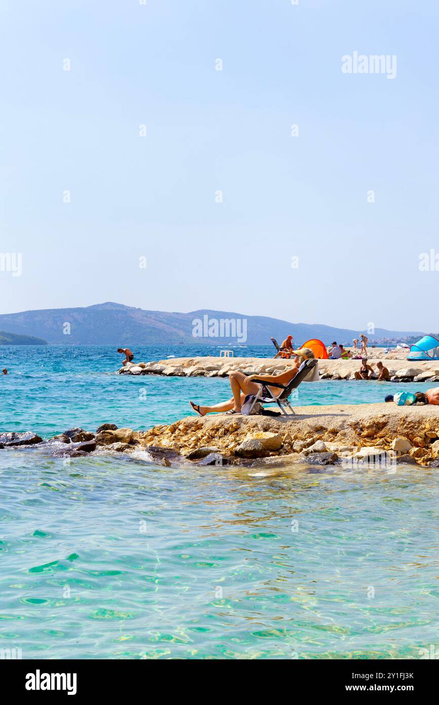 Donna che prende il sole alla spiaggia di Rozac (Plaža Rožac), isola di Ciovo sul mare Adriatico vicino a Traù, Croazia Foto Stock