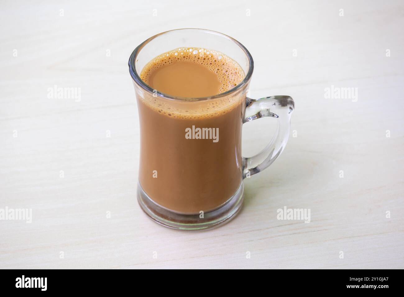 Una tazza di tè al latte caldo o di dudh cha in una tazza di vetro posta su una superficie di legno chiaro. Foto Stock