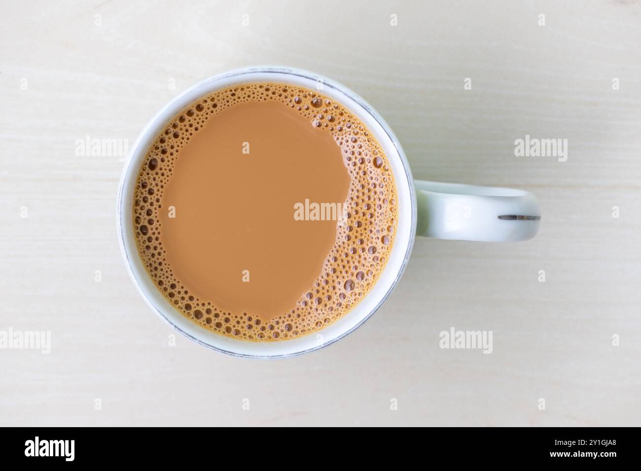 Una tazza di tè al latte o di dudh cha in una tazza di ceramica su una superficie di legno chiaro. Vista dall'alto. Foto Stock