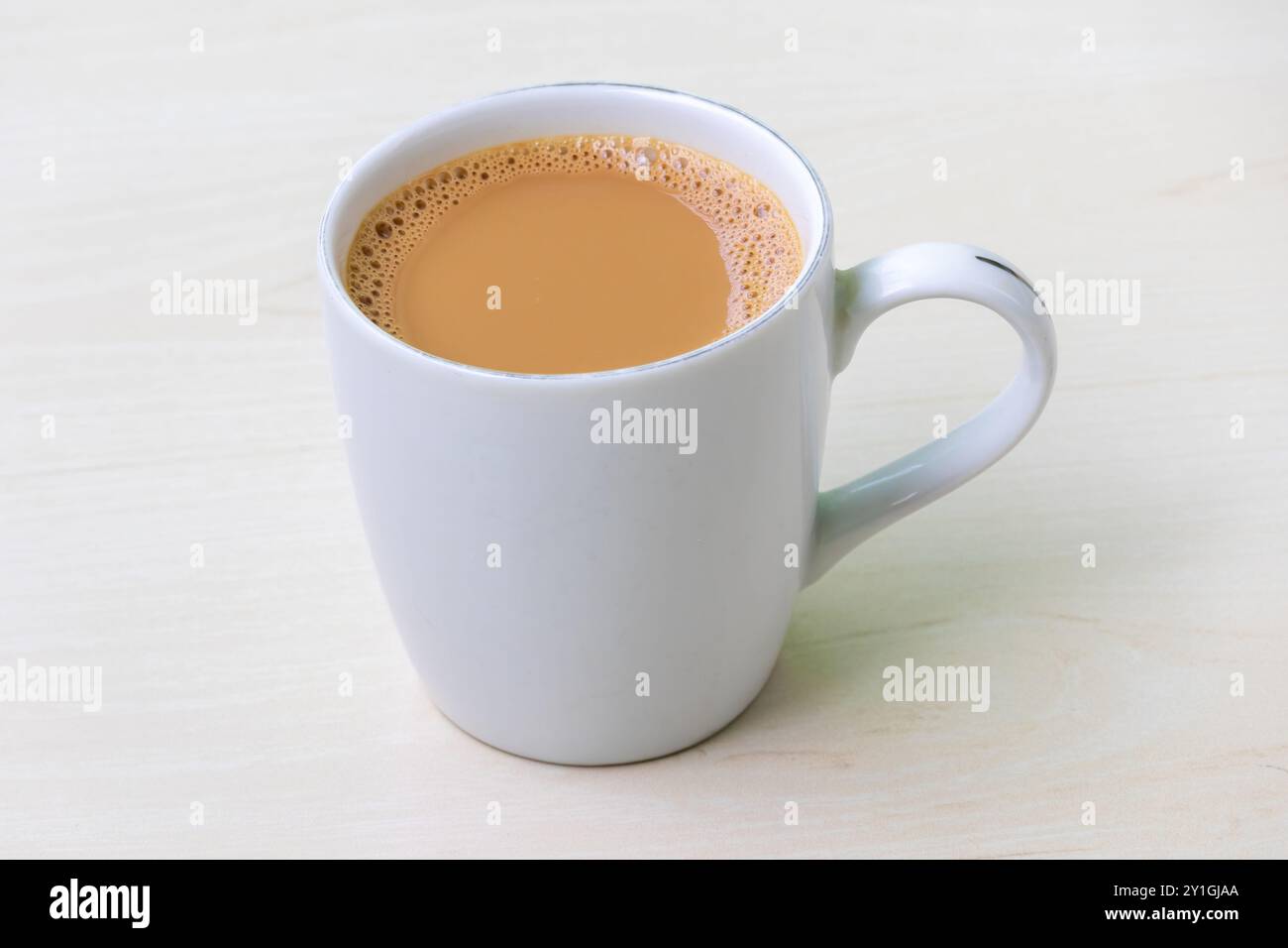 Una tazza di tè al latte caldo o di dudh cha in una tazza di ceramica bianca su una superficie di legno chiaro. Foto Stock