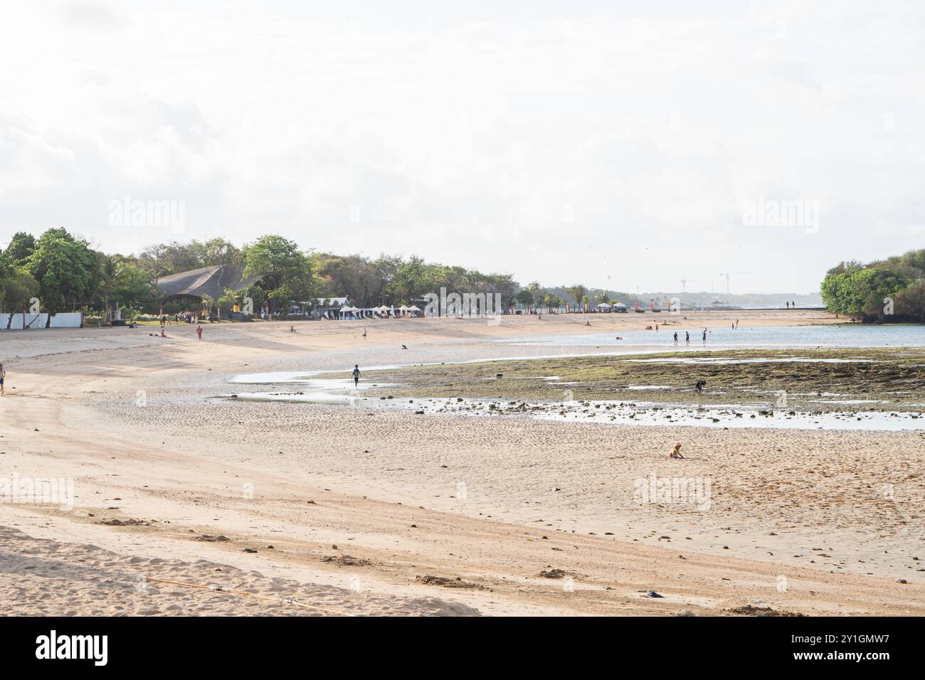 Una vista panoramica di una spiaggia rocciosa durante la bassa marea, con l'oceano sullo sfondo. Le onde dolci si infrangono sulla riva e alcune persone possono essere viste esplorare Foto Stock