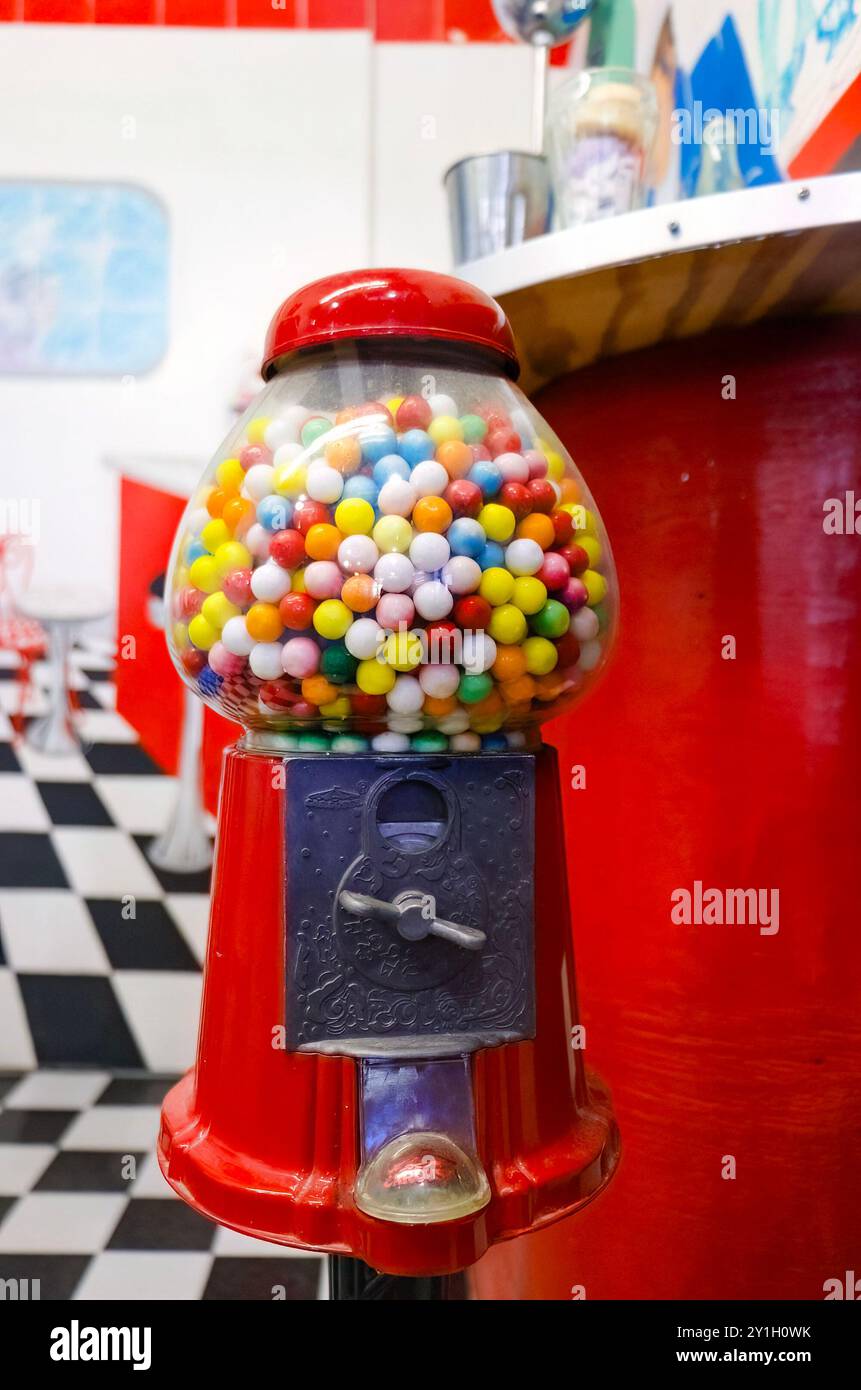 Macchinetta da gumball rossa d'epoca piena di gomme colorate in piedi in un ristorante retrò con pavimento a scacchi bianco e nero e decorazioni rosse. Foto Stock