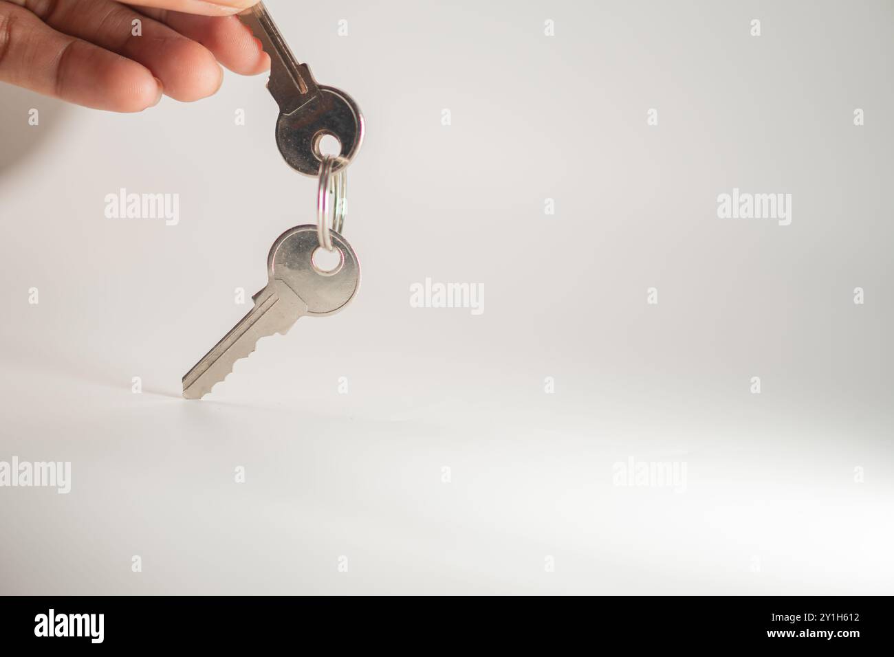 Una mano che regge un set di chiavi con un portachiavi su uno sfondo semplice. Le chiavi sono lucenti e metalliche, riflettono la luce. Foto Stock