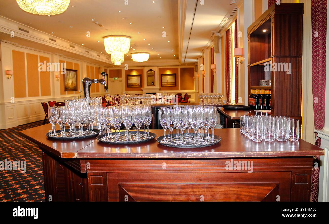 Un'area bar splendidamente arredata in una sala banchetti, con vassoi multipli di bicchieri da vino frizzante pulito. Il decor elegante include lampadari e Foto Stock