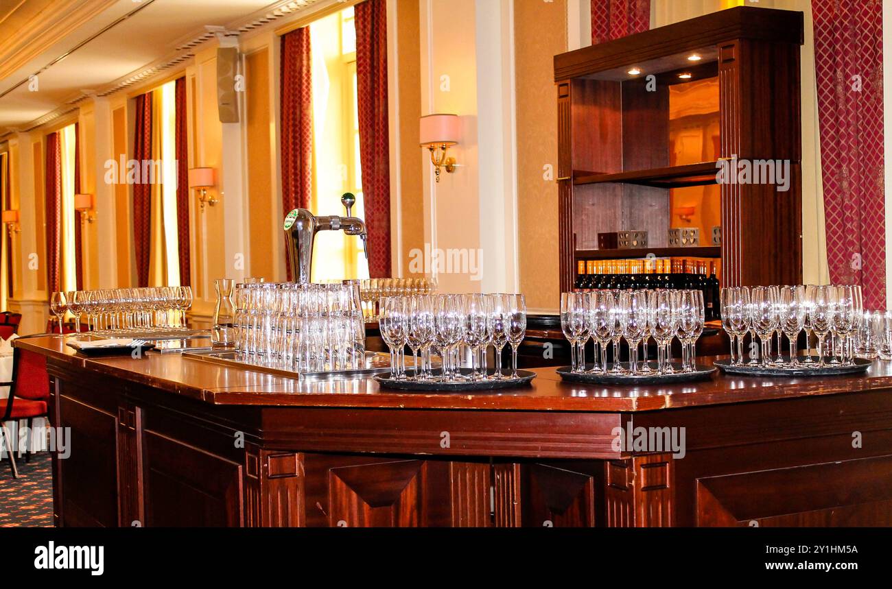Un'area bar splendidamente arredata presenta numerosi bicchieri scintillanti su un bancone in legno lucido, con un decor elegante e una luce soffusa sullo sfondo Foto Stock