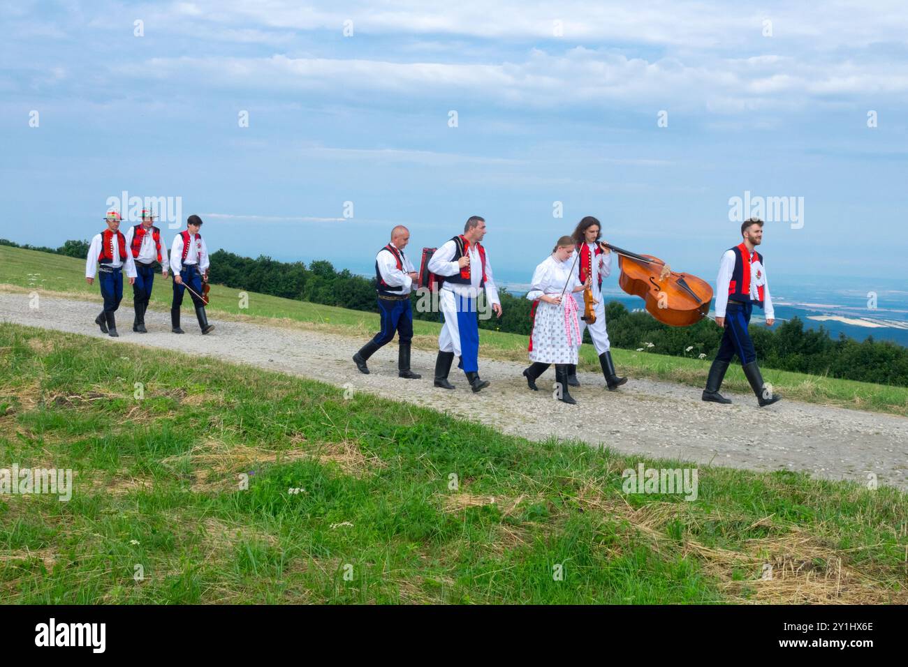 Un gruppo di persone in abbigliamento tradizionale cammina su un sentiero rurale con strumenti musicali in una giornata limpida nella Repubblica Ceca Foto Stock
