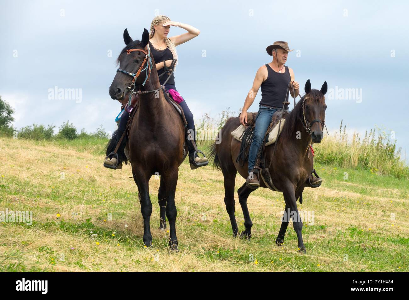 Due persone a cavallo attraverso un campo erboso, una che guarda in lontananza mentre l'altra tiene le redini Foto Stock