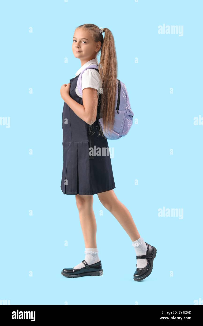 Una bambina carina in uniforme scolastica su sfondo blu Foto Stock