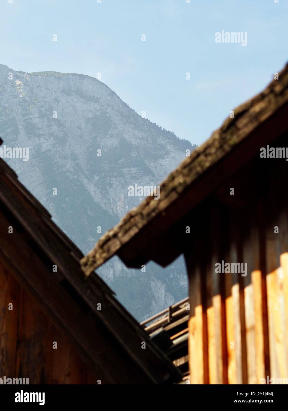 Uno scatto panoramico con una montagna a picco in lontananza, incorniciata da due rustici tetti in legno in pendenza, che catturano la bellezza del paesaggio naturale Foto Stock