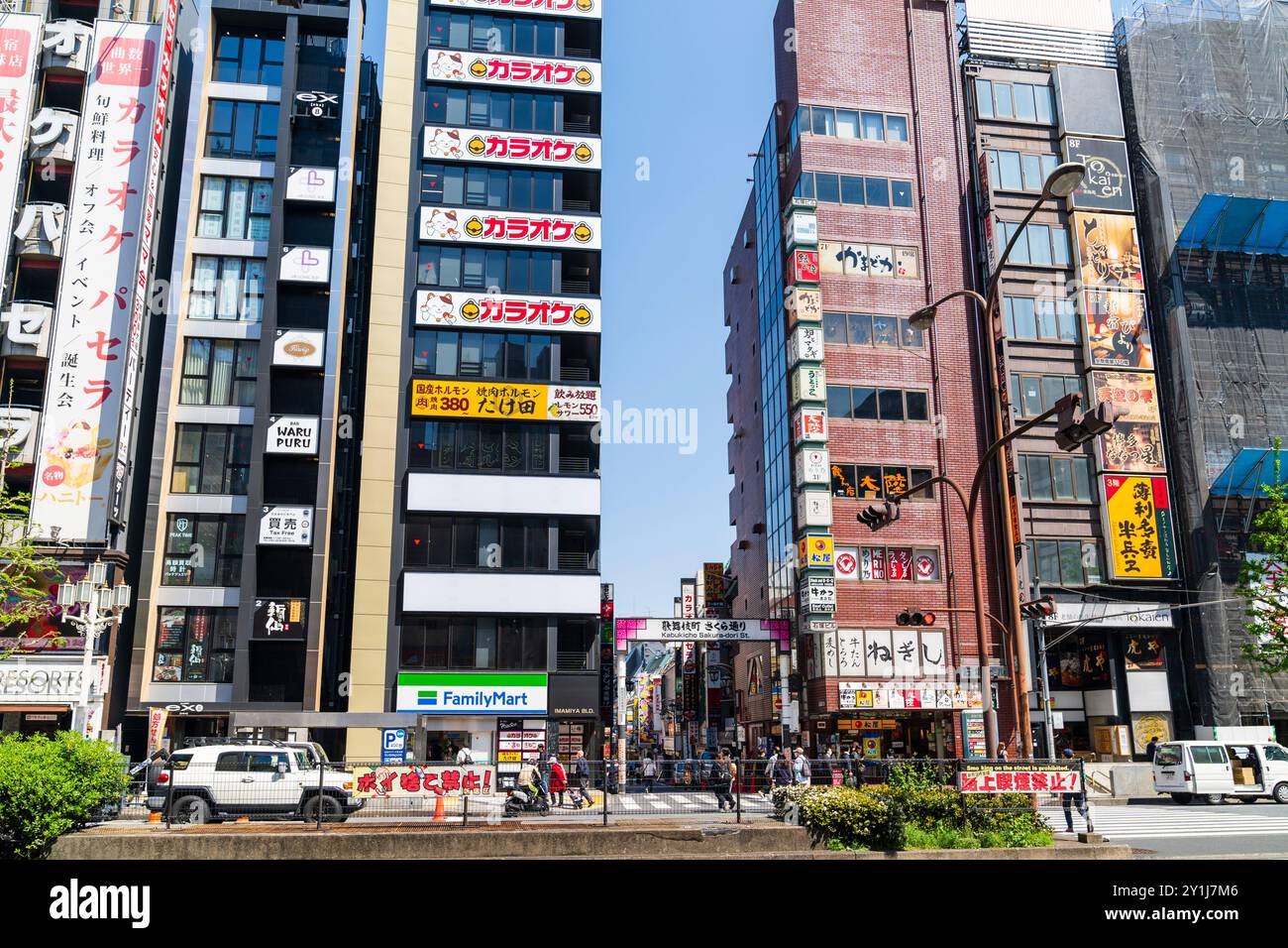 Alti edifici e negozi a Shinjuku dall'altro lato della strada principale, nel mezzo c'è la via kabukicho Sakura Dori e il suo cartello sospeso. Di giorno. Foto Stock