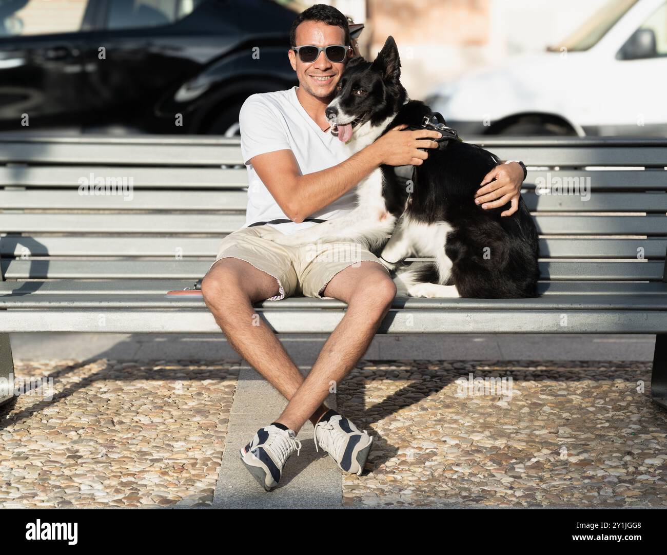Un uomo siede su una panchina con il suo cane. L'uomo sorride e il cane lo guarda. La scena è tranquilla e felice Foto Stock