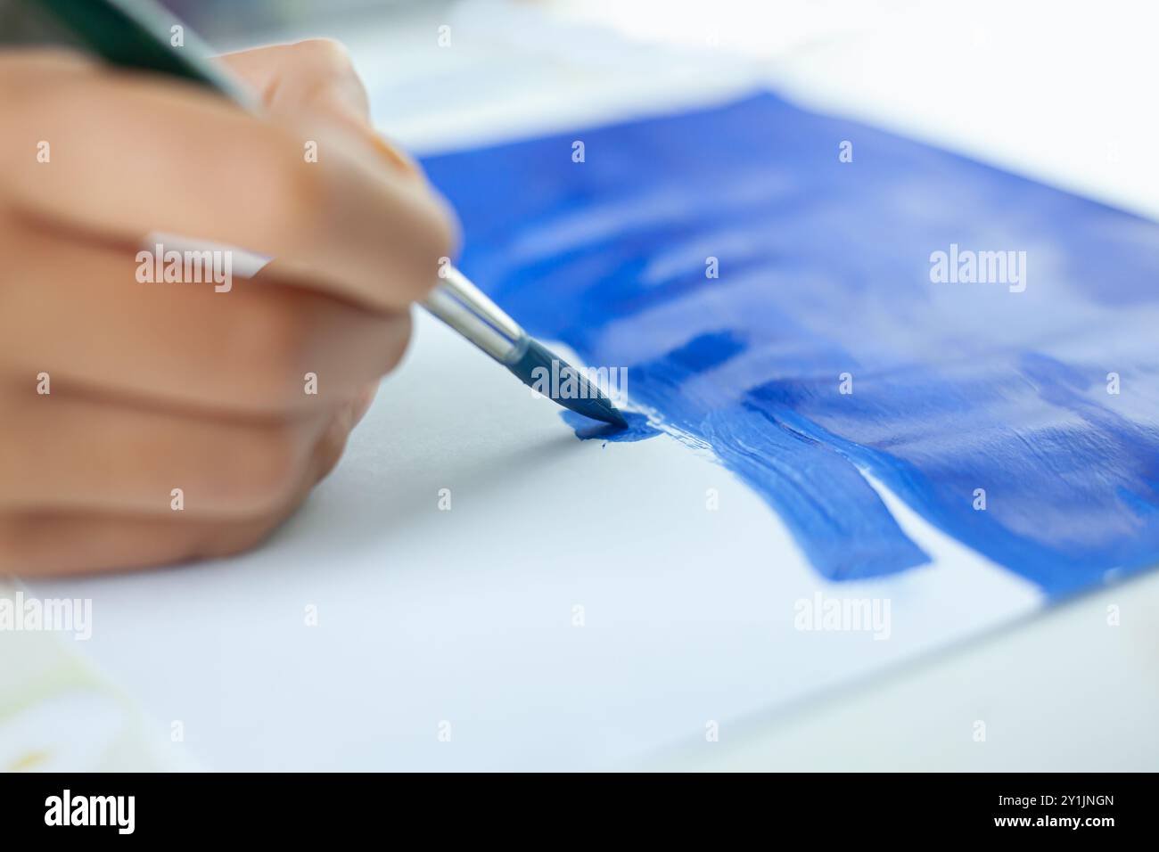 bambini che dipingono con un pennello blu su un foglio di carta bianco. Foto Stock