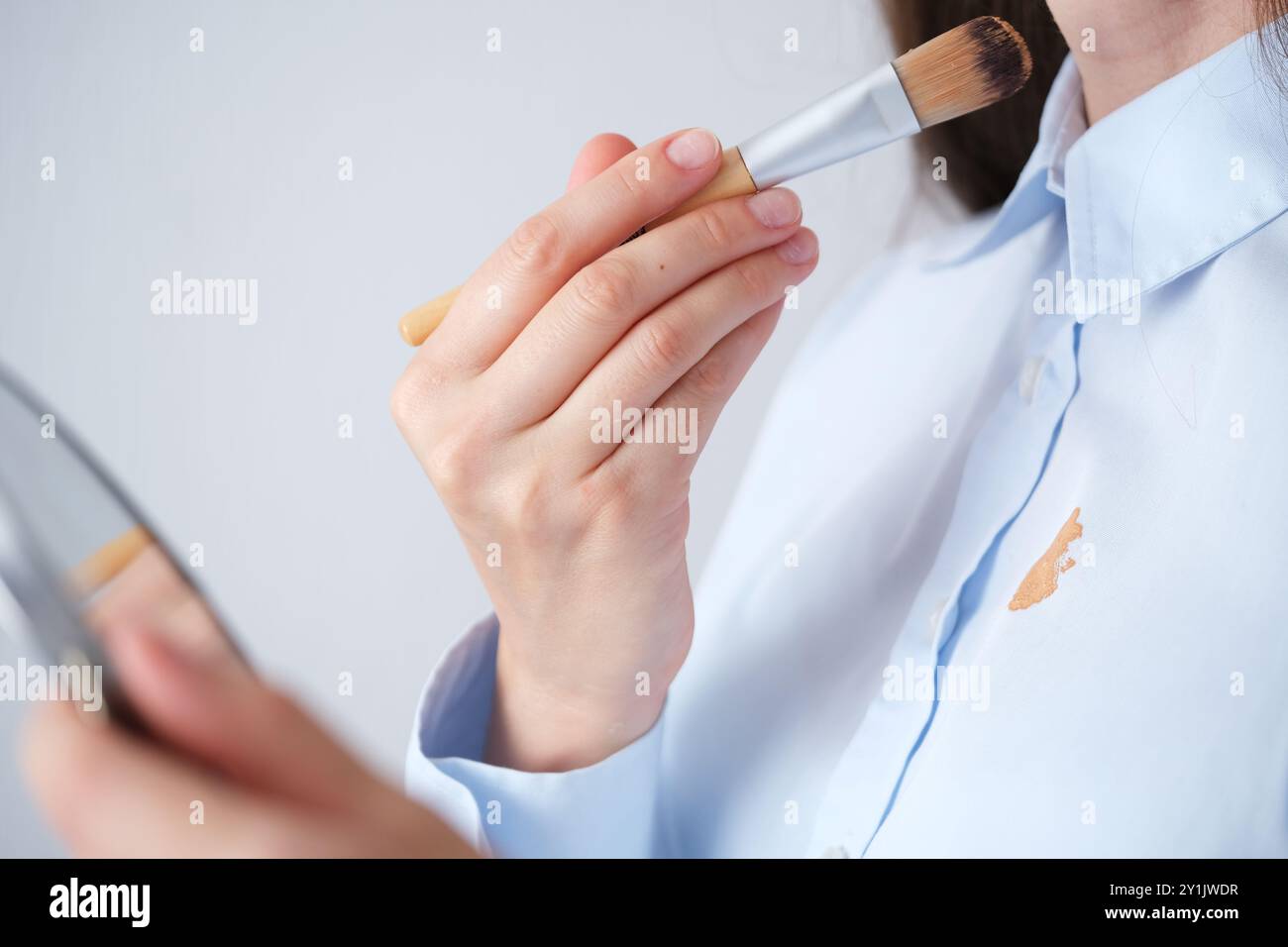 Donna che applica le fondamenta con una spazzola indossando una camicia azzurra in una stanza ben illuminata durante il giorno. concetto di colorazione per la vita quotidiana. Alta qualità p Foto Stock