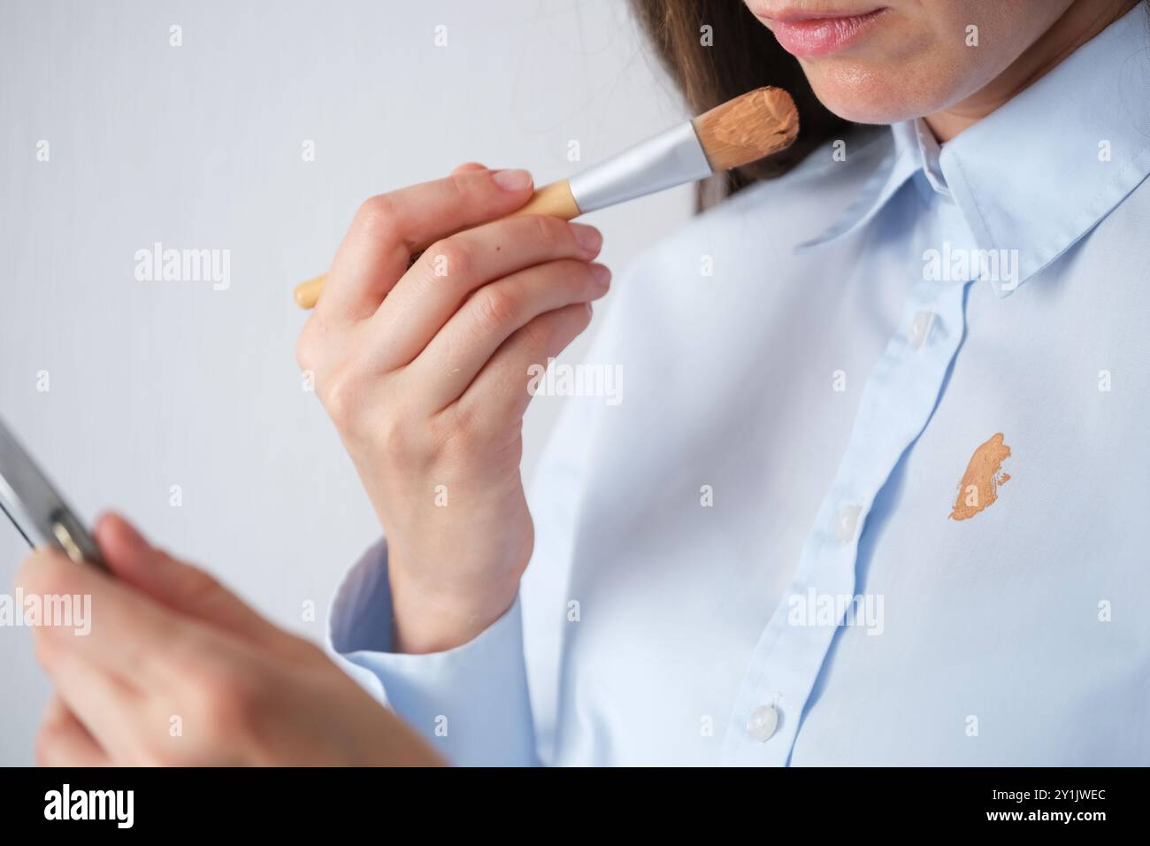 Donna che applica le fondamenta con una spazzola indossando una camicia azzurra in una stanza ben illuminata durante il giorno. concetto di colorazione per la vita quotidiana. Alta qualità p Foto Stock