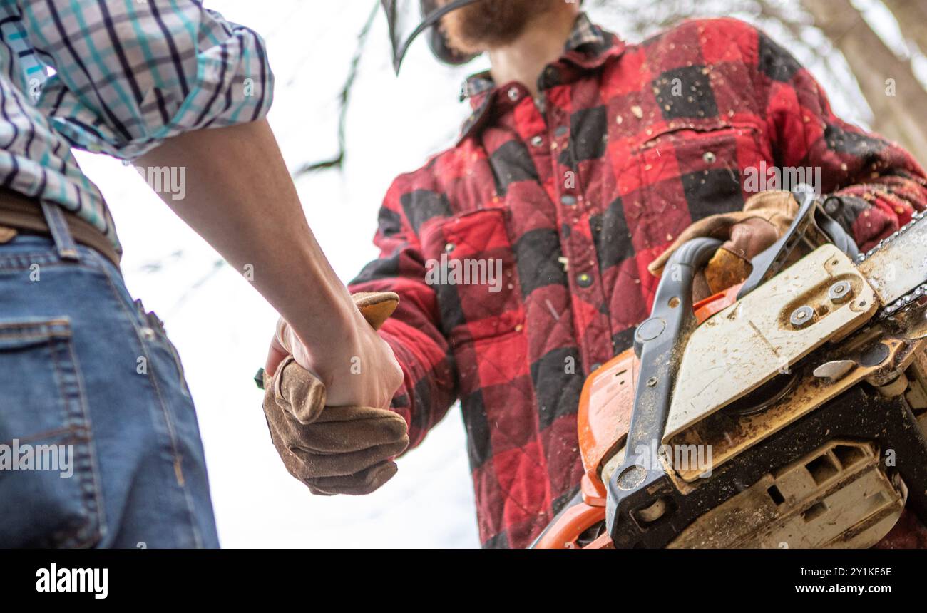 Il boss stringendo la mano con il duro lavoro sawyer con motosega in una giornata invernale, ha visto spargere polvere sulla camicia rossa dei lavoratori a quadri Foto Stock