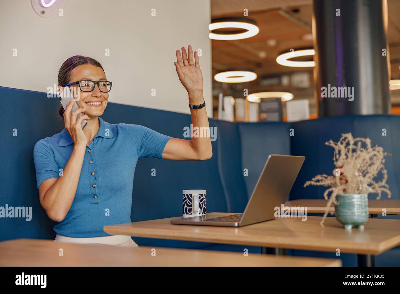 Una donna è impegnata in una telefonata in uno spazio di lavoro vivace, che mette in evidenza un'atmosfera trafficata ma rilassata Foto Stock