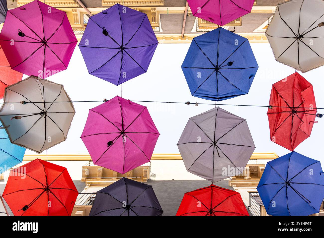 Ombrelli vibranti appesi sulla strada di Catania, Sicilia. Colorata installazione di arte urbana che fornisce ombra e interesse visivo. Prospettiva unica da Foto Stock