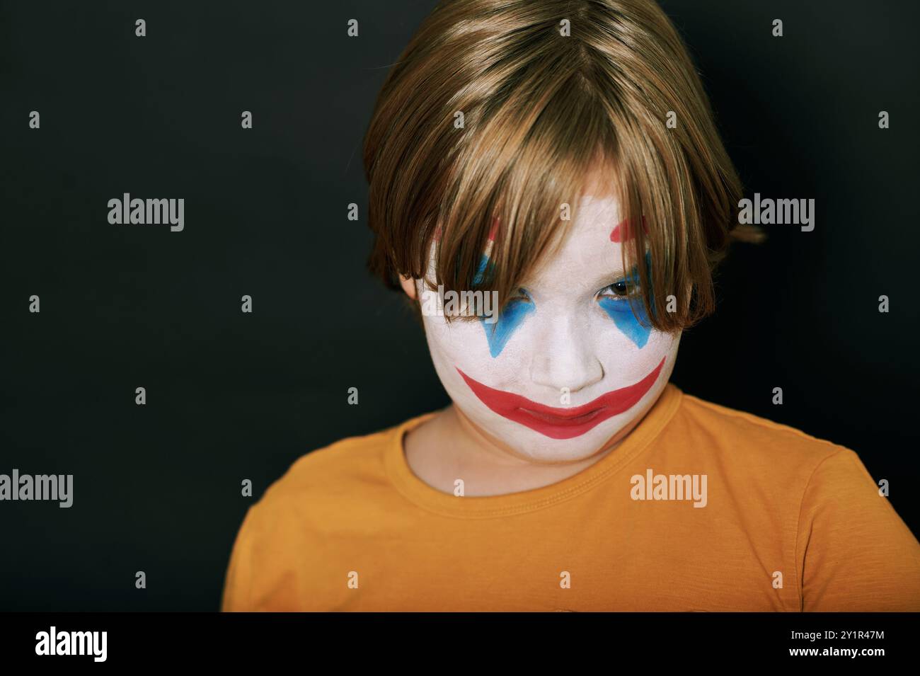 Ritratto di Halloween di un ragazzino che indossa la pittura del viso o il trucco di Joker, che posa su sfondo nero dello studio Foto Stock