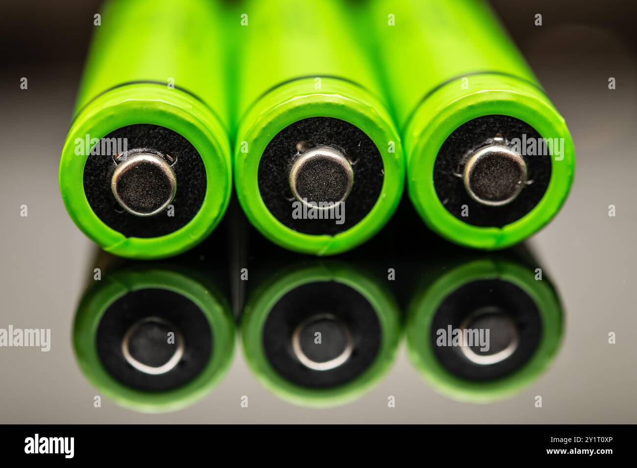 Tre batterie ricaricabili AAA verdi luminose posizionate una accanto all'altra, che si riflettono su una superficie in vetro, simboleggiano l'avanzata tecnologia ecologica ed ecocompatibile Foto Stock