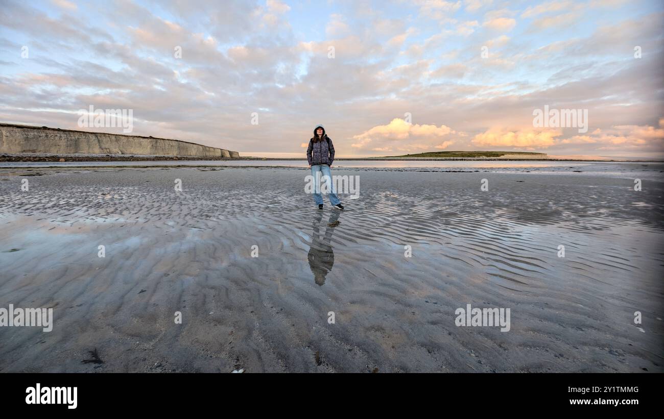 Donna escursionista con zaino in spalla che gode del paesaggio costiero del tramonto sulla spiaggia sabbiosa di Silverstrand, Galway, Irlanda, avventura e stile di vita, persone nella natura Foto Stock