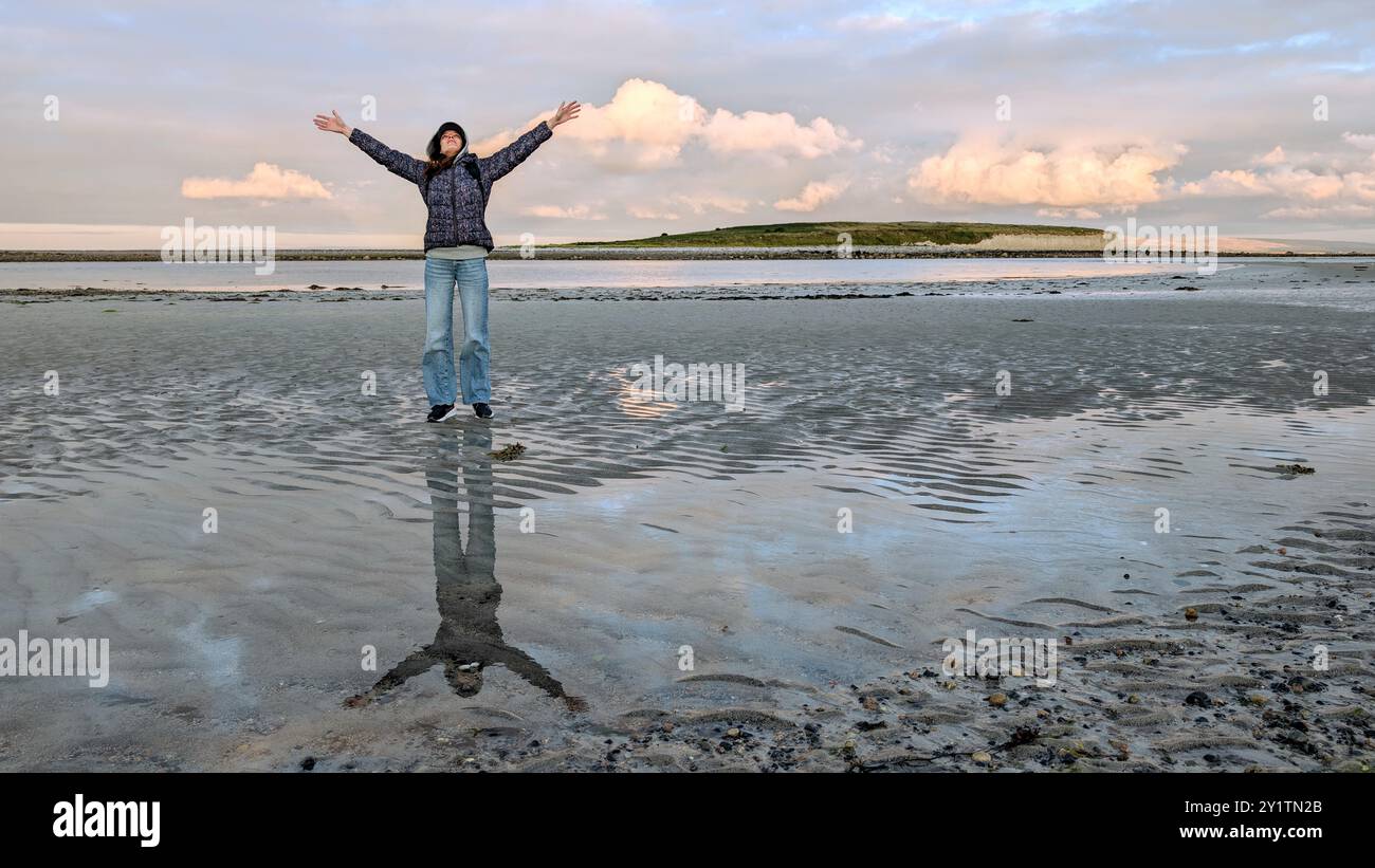 Donna escursionista con zaino in spalla che gode del paesaggio costiero del tramonto sulla spiaggia sabbiosa di Silverstrand, Galway, Irlanda, avventura e stile di vita, persone nella natura Foto Stock