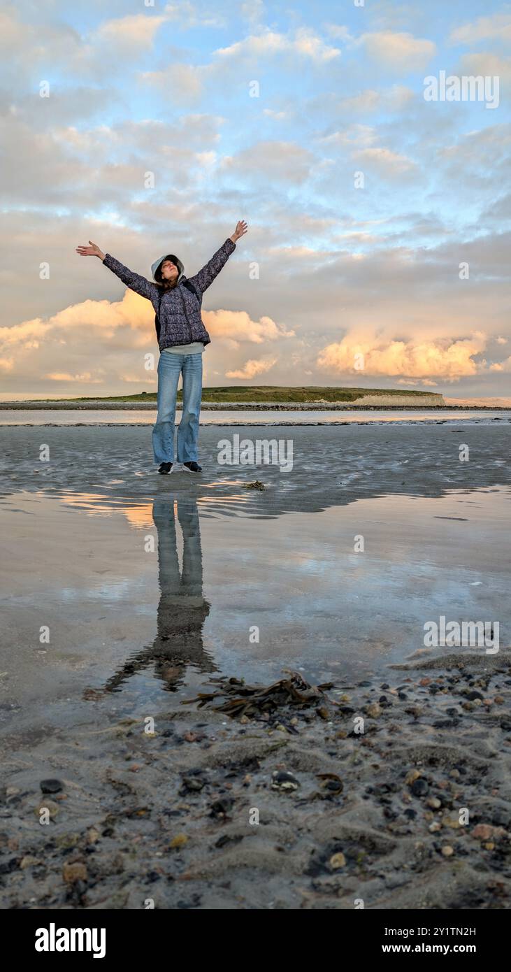 Donna escursionista con zaino in spalla che gode del paesaggio costiero del tramonto sulla spiaggia sabbiosa di Silverstrand, Galway, Irlanda, avventura e stile di vita, persone nella natura Foto Stock