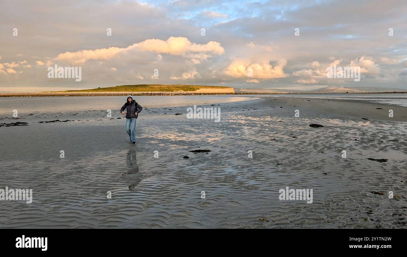 Donna escursionista con zaino in spalla che gode del paesaggio costiero del tramonto sulla spiaggia sabbiosa di Silverstrand, Galway, Irlanda, avventura e stile di vita, persone nella natura Foto Stock