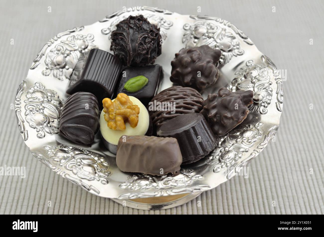 Diversi tipi di praline di cioccolato su un piatto d'argento, primo piano, isolate su sfondo bianco Foto Stock