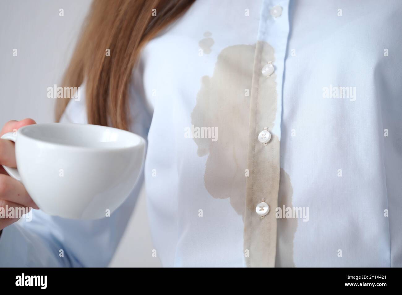 Una persona irriconoscibile con una camicia azzurra versa caffè. Macchie di caffè marrone sporche sui vestiti. concetto di colorazione della vita quotidiana . Foto di alta qualità Foto Stock