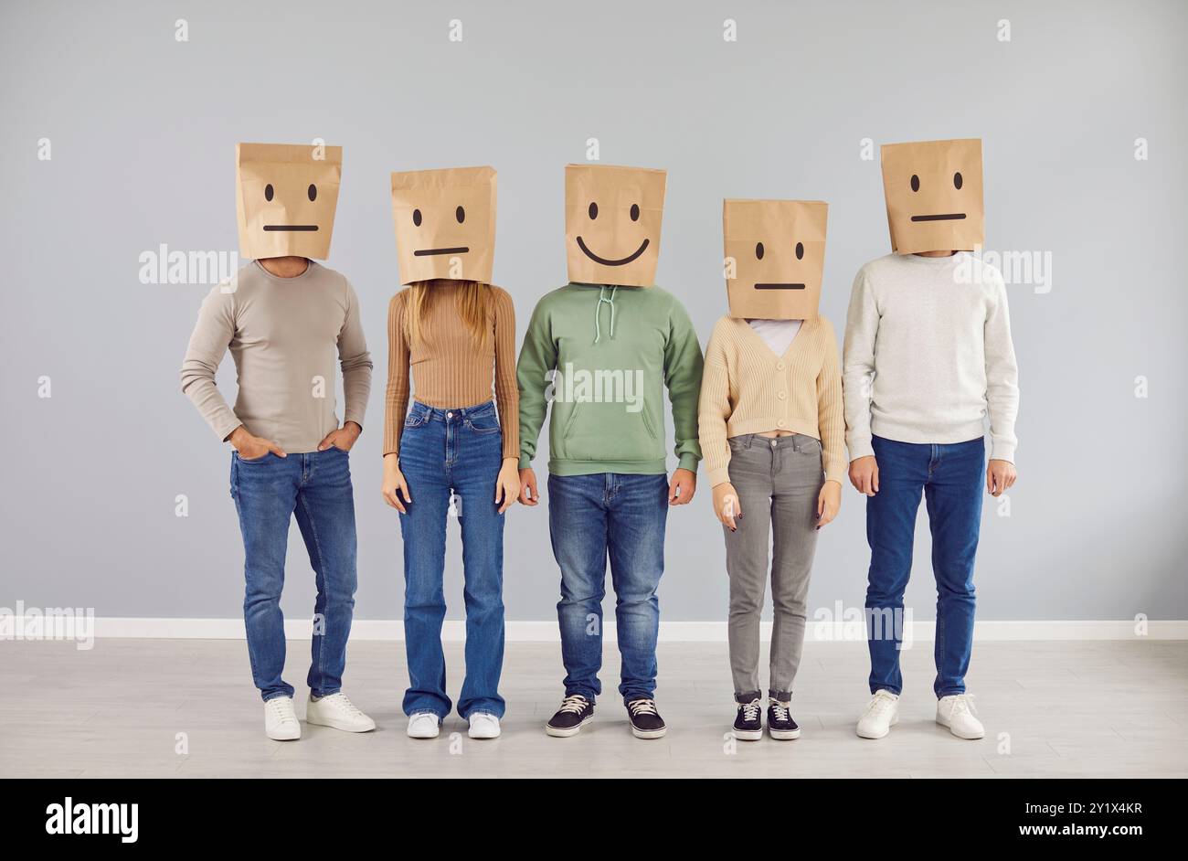 Persona sorridente felice e gruppo di persone gravi e indifferenti con sacchetti di carta sulla testa Foto Stock