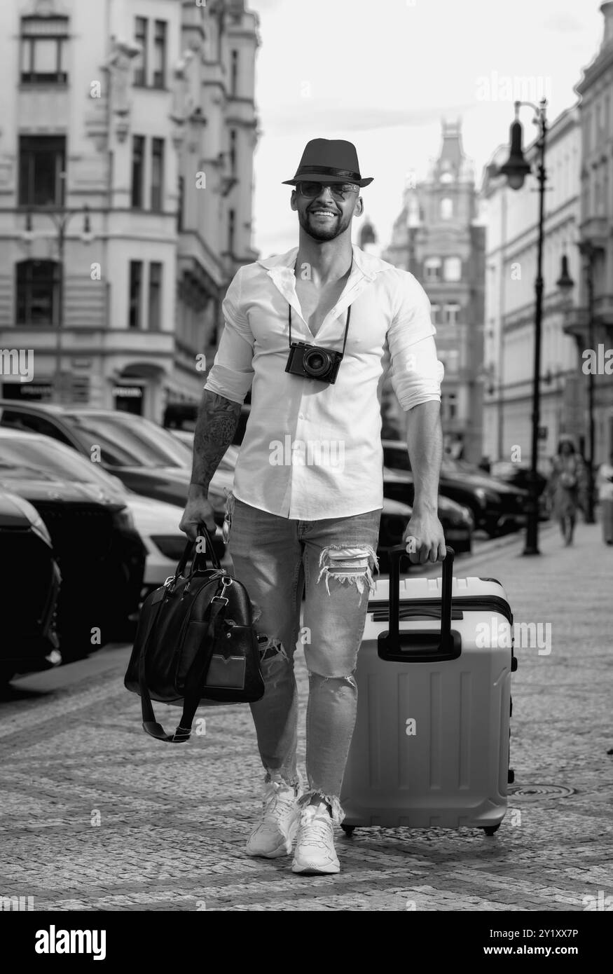 Viaggiatore studente o giovane turista. Uomo viaggiatore con borsa da viaggio all'aperto. Ritratto del giovane uomo caucasico in cappello e occhiali da sole in vacanza estiva. Foto Stock