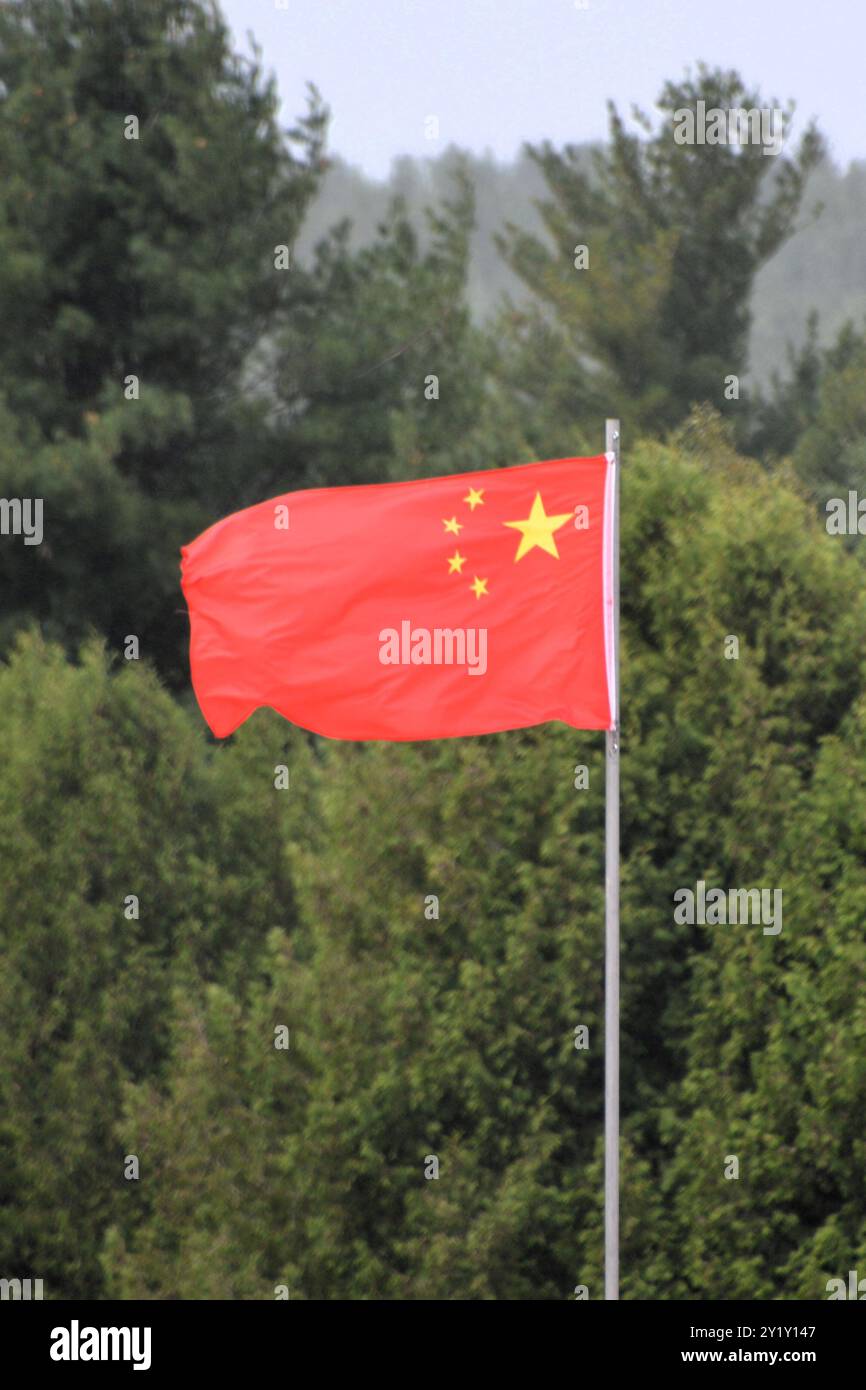La bandiera nazionale della Repubblica Popolare Cinese, chiamata anche bandiera Rossa a cinque stelle, sventolava in aria su un palo con alberi sullo sfondo. Foto Stock