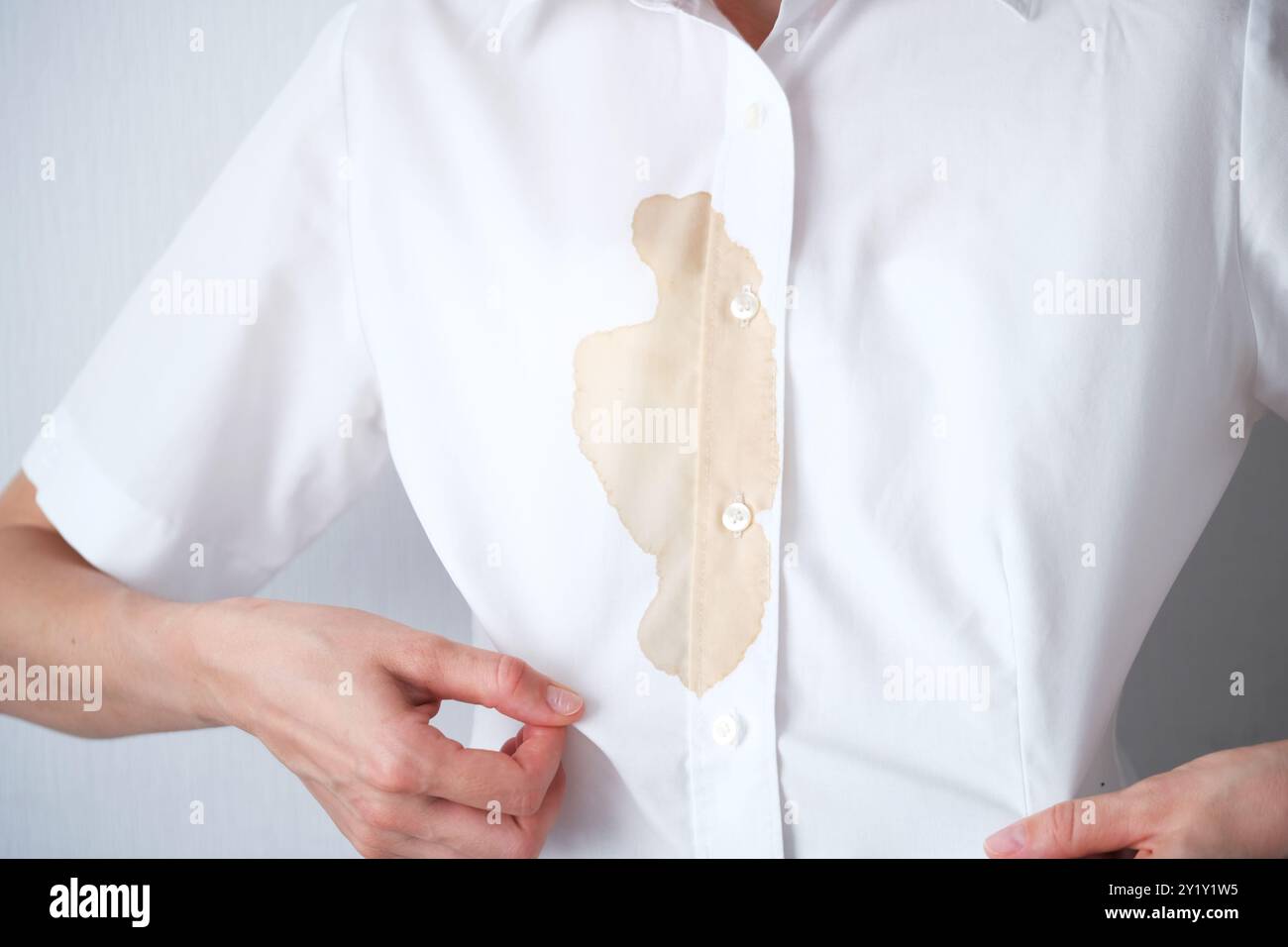 Persona irriconoscibile con una camicia bianca chiara che mostra una macchia marrone in un ambiente interno informale. Bevanda o salsa marrone sporca sui vestiti. spazio per il testo . H Foto Stock