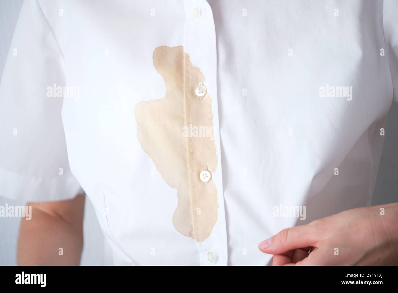 Persona irriconoscibile con una camicia bianca chiara che mostra una macchia marrone in un ambiente interno informale. Bevanda o salsa marrone sporca sui vestiti. spazio per il testo . H Foto Stock