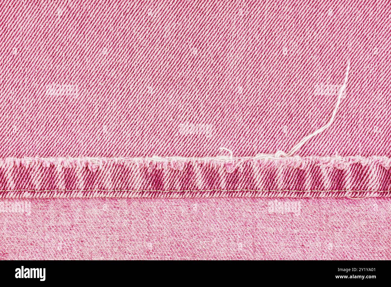 Pantaloni in jeans in denim rosa con bordo scabro su fondo in tessuto jean, primo piano, macro. Jeans strappati, distrutti strappati. Sfondo, sfondo, dettagli di design. Foto Stock