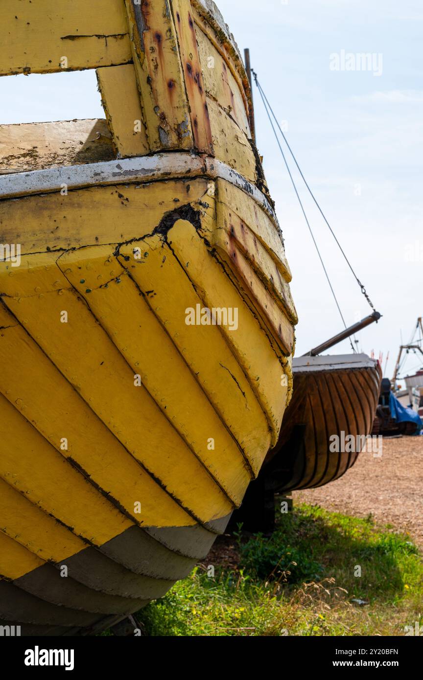 Vecchia barca da pesca in legno di colore giallo pallido sulla riva di Hastings, in una giornata di sole con attrezzature arrugginite, a poppa Foto Stock