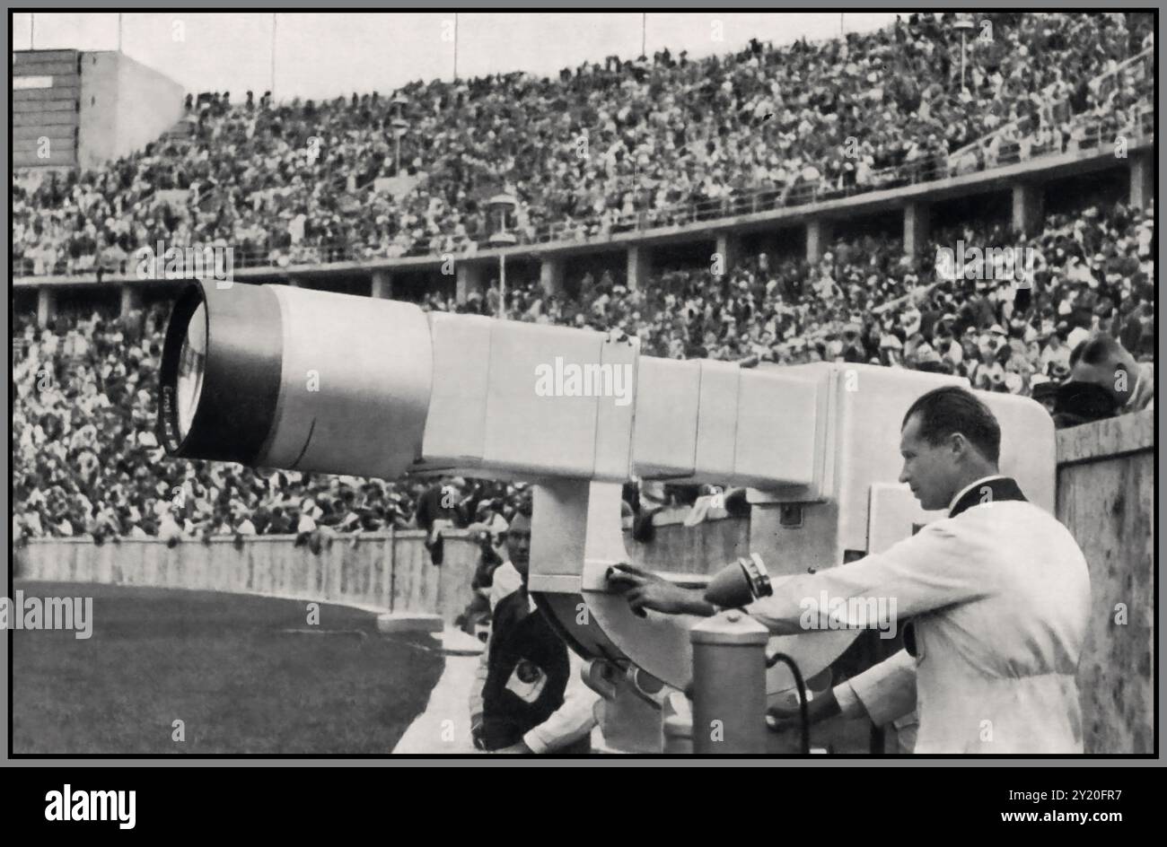 Le Olimpiadi di Berlino del 1936 hanno segnato un momento storico nella trasmissione, in quanto sono state le prime Olimpiadi ad essere trasmesse in diretta televisiva. Telefunken, un'azienda tedesca pioniera nell'elettronica, ha svolto un ruolo cruciale in questa innovazione tecnologica. L'immagine di un tecnico televisivo Telefunken che regola l'obiettivo durante la trasmissione in diretta dei Giochi, lavorando attentamente sul punto di vista e sull'ingrandimento, simboleggia l'innovazione tecnologica del tempo. Le loro fotocamere, dotate di obiettivi specializzati, hanno catturato l'azione per la trasmissione in diretta, offrendo un'esperienza visiva senza precedenti. Foto Stock