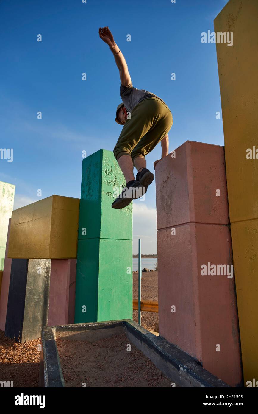 Uomo ispanico che salta tra blocchi colorati di cemento praticando il parkour e la scena urbana che trasmette il concetto di movimento del corpo e benessere. Tramonto Foto Stock