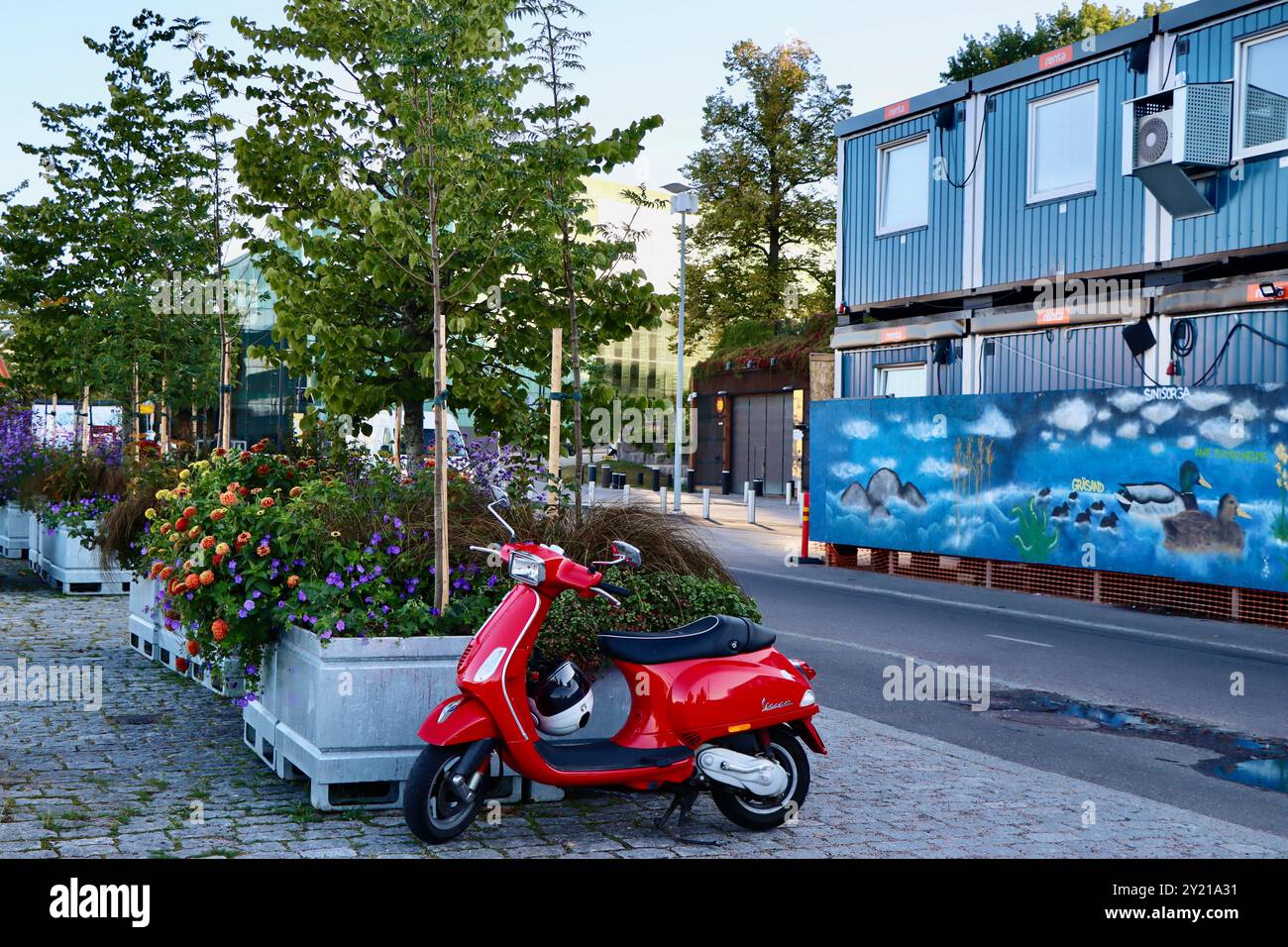 Una Vespa rossa parcheggiata nel parco di Töölönlahti presso le abbondanti vasi di fiori, Helsinki, Finlandia, agosto 2024 Foto Stock