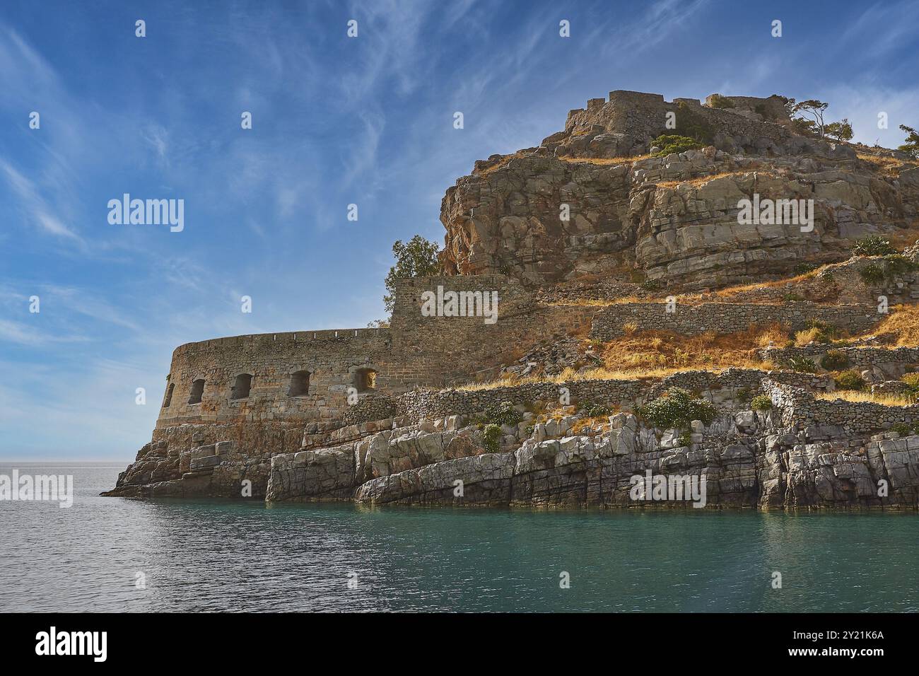 Muro di pietra nella scena costiera rocciosa in riva al mare con cielo azzurro e acque calme, la Fortezza del Mare di Venezia, l'isola di Leper, Spinalonga, la baia di Elounda, Mirabel Foto Stock
