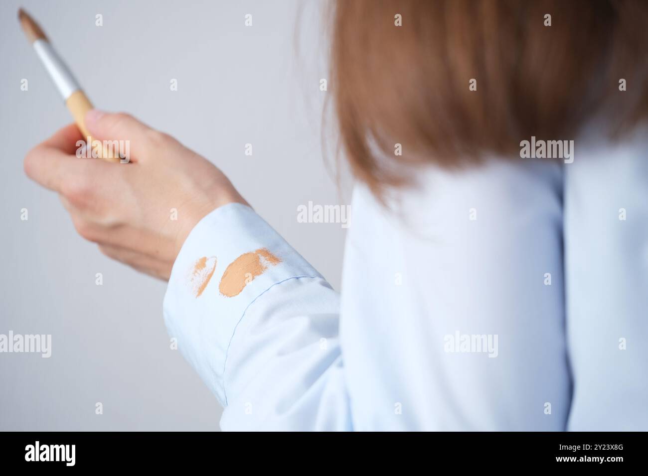 Donna che applica le fondamenta con una spazzola indossando una camicia azzurra in una stanza ben illuminata durante il giorno. concetto di colorazione per la vita quotidiana. Alta qualità p Foto Stock
