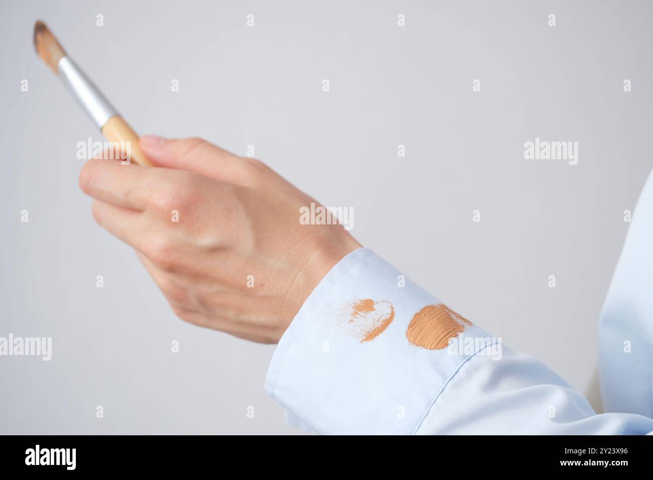 Donna che applica le fondamenta con una spazzola indossando una camicia azzurra in una stanza ben illuminata durante il giorno. concetto di colorazione per la vita quotidiana. Alta qualità p Foto Stock