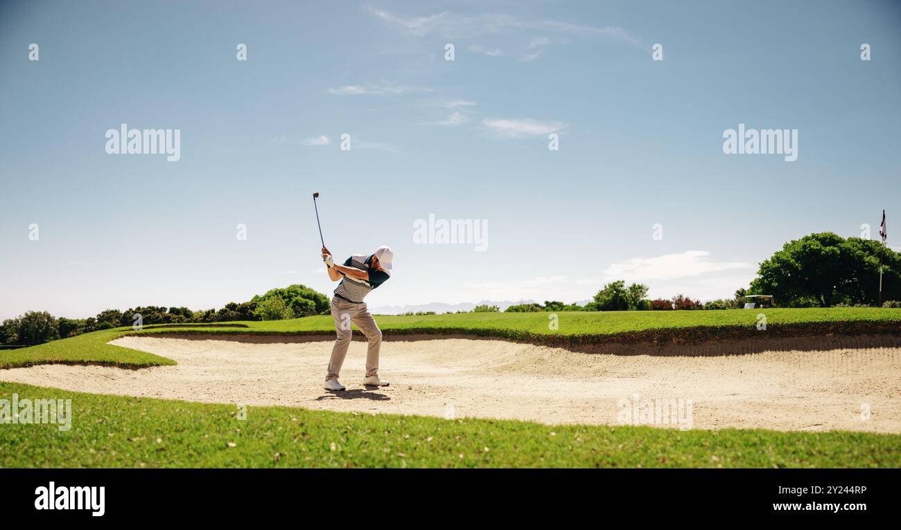 Un golfista maschio che fa oscillare abilmente una mazza da golf per sfuggire a un bunker durante una partita competitiva, catturando determinazione e precisione. Foto Stock