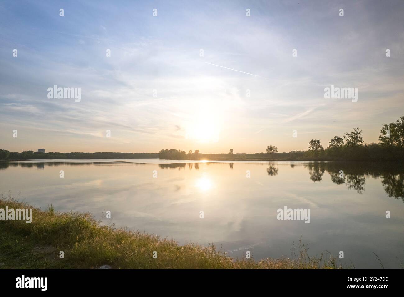 Il tranquillo sentiero di ghiaia si snoda lungo la tranquilla riva di un lago al tramonto, con una luce dorata che si riflette nelle acque calme, creando una scena tranquilla, po R. Foto Stock